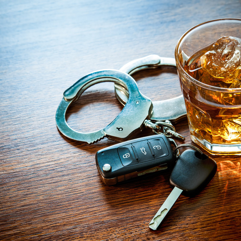 glass of alcohol next to car keys and handcuffs
